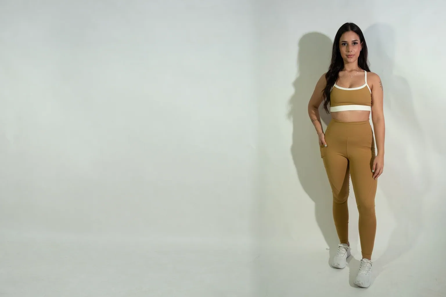 Modelo com conjunto caramelo de top com vivo branco e legging, em estúdio